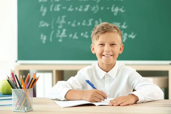En liten gutt som gjør lekser i klasserommet – stockfoto