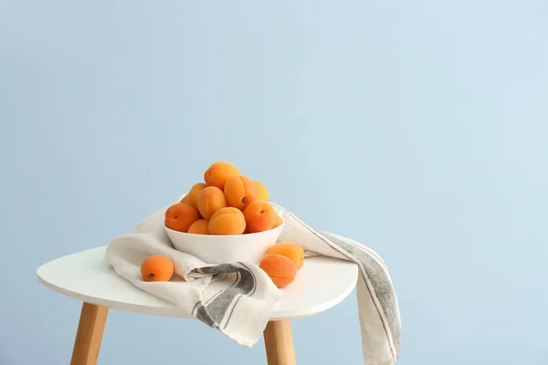 Bowl with tasty ripe apricots on table against color background — Stock Photo, Image