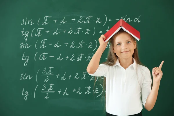 Little girl with raised index finger near school blackboard in classroom