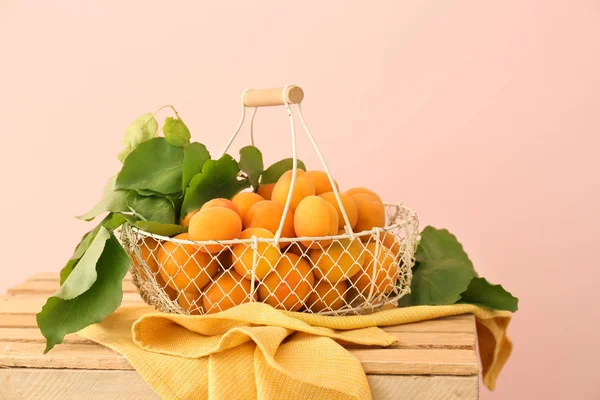 Basket with tasty ripe apricots on wooden box against color background — Stock Photo, Image