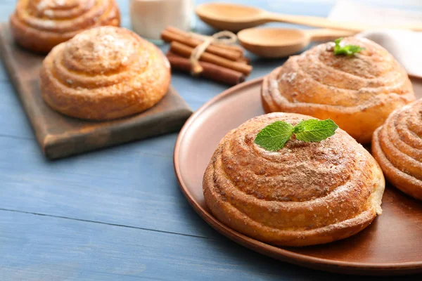 Ahşap masa üzerinde lezzetli tarçınlı çörek ile plaka — Stok fotoğraf