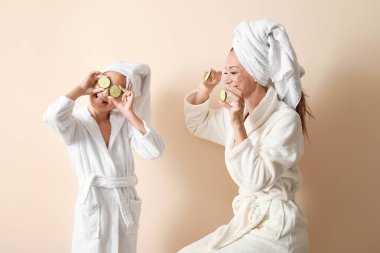 Bornozlu kızı ve hafif arka planda salatalık dilimleri ile mutlu anne portresi