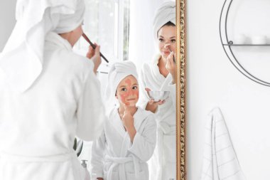 Banyoda aynanın yanındaki yüze maske uygulayan anne