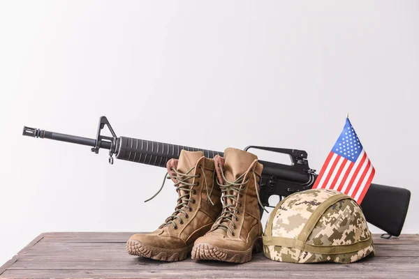 テーブルの上に軍のヘルメット、ブーツ、アサルトライフルとアメリカの旗 — ストック写真