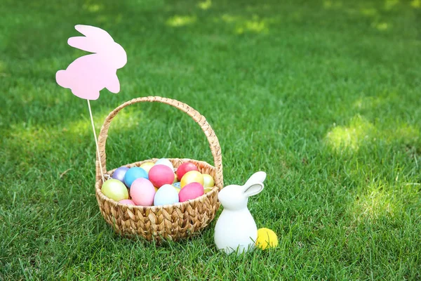 Cesta com ovos de Páscoa e coelho na grama ao ar livre — Fotografia de Stock