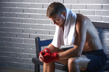 Tuğla duvara karşı bankta oturan güçlü erkek boksör