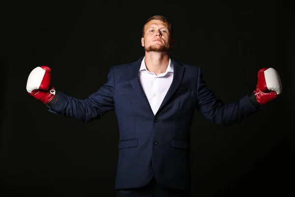 Businessman in boxing gloves against dark background