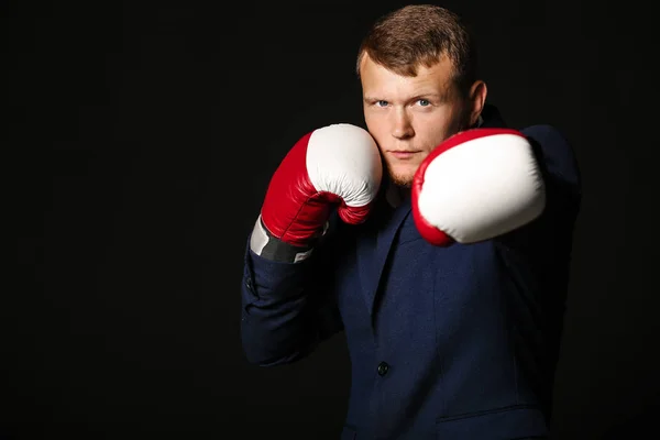 Businessman in boxing gloves against dark background