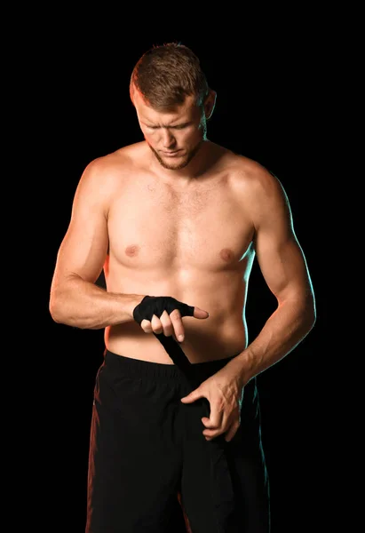 Boxeador masculino fuerte aplicando muñequeras sobre fondo oscuro — Foto de Stock