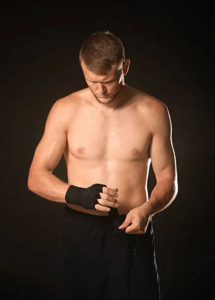 Boxeador masculino fuerte aplicando muñequeras sobre fondo oscuro — Foto de Stock