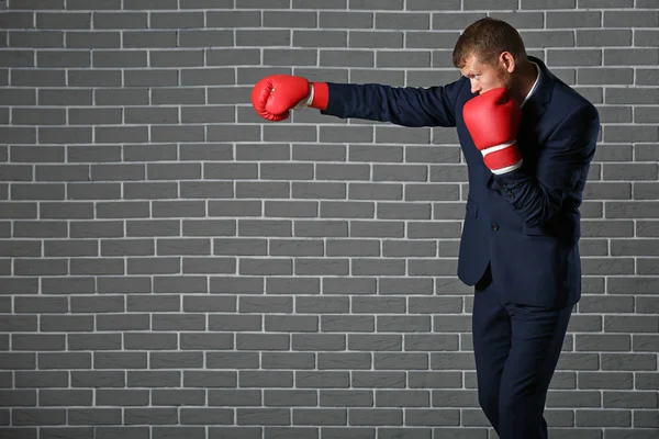 Businessman in boxing gloves against brick wall