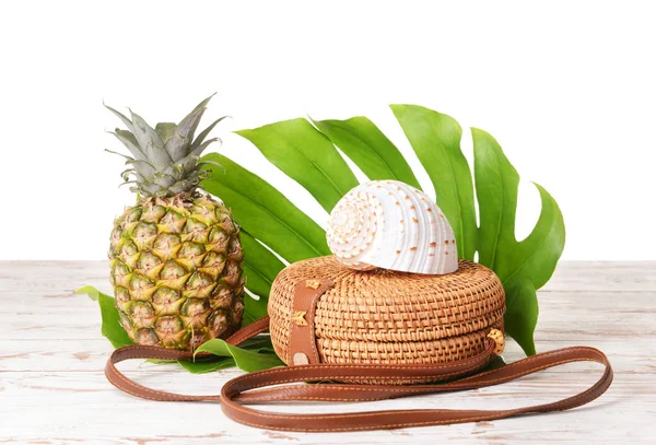 Bag, pineapple, sea shell and tropical leaf on table against white background — Stock Photo, Image