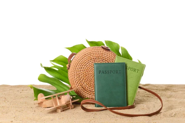 Beach bag, passports, toy airplane and tropical leaf on sand against white background — Stock Photo, Image