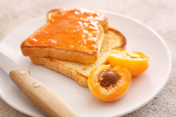 Tasty apricot jam with bread slices on plate, closeup — Stock Photo, Image