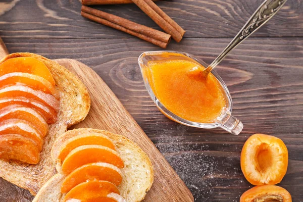 Bread slices with tasty apricot jam on wooden table — Stock Photo, Image