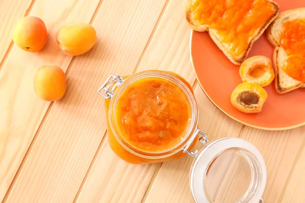 Sklenice s chutnými meruňkové marmeládou a chlebem na dřevěném stole — Stock fotografie
