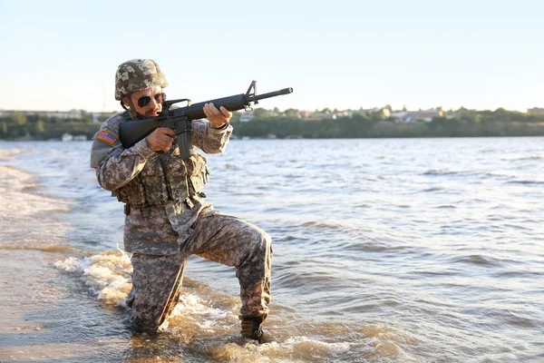 Soldier in camouflage taking aim near river — Stock Photo, Image