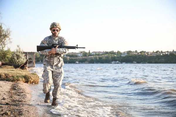 Soldato in camuffamento con fucile d'assalto vicino al fiume — Foto Stock