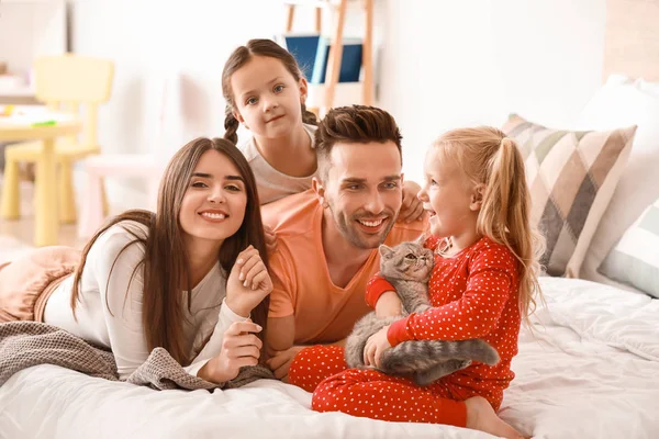 Gelukkige familie met schattige kat op bed thuis — Stockfoto
