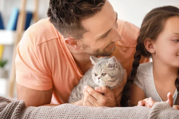 Família feliz com gato bonito deitado na cama em casa — Fotografia de Stock