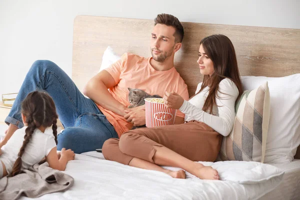 Happy family with cute cat watching TV on bed at home — Stock Photo, Image