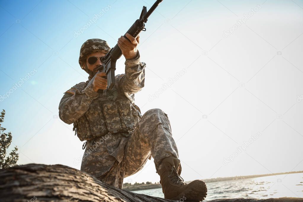 Soldier in camouflage taking aim near river