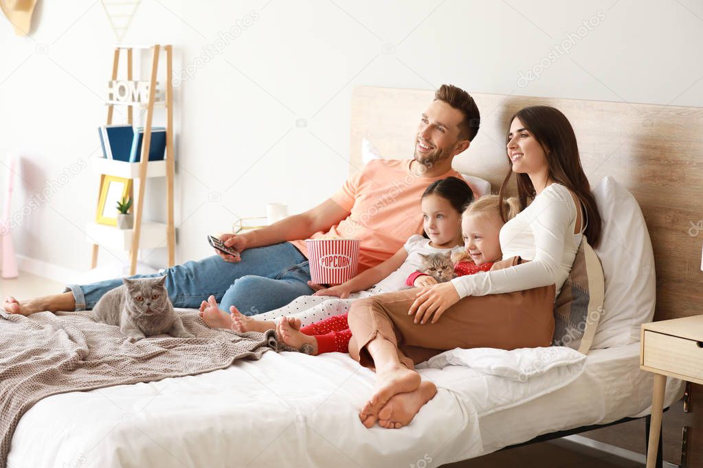 Happy family with cute cats watching TV on bed at home