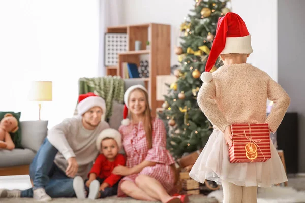 Liten flicka med gåva och hennes familj hemma på julafton — Stockfoto