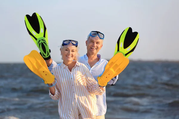 Happy mature couple with snorkeling masks and paddles having fun at sea resort — Stock Photo, Image