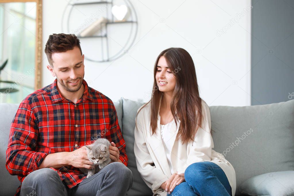 Happy couple with cute cat resting at home