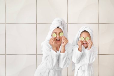 Anne ve bornoz onun küçük kızı ve beyaz arka plan karşı salatalık dilimleri ile