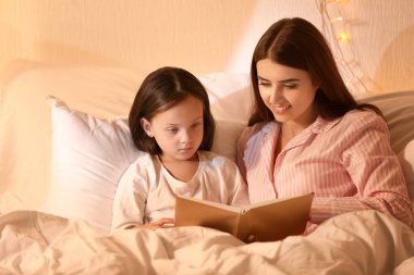 Anne ve küçük kızı evde yatmadan önce hikaye okuyor
