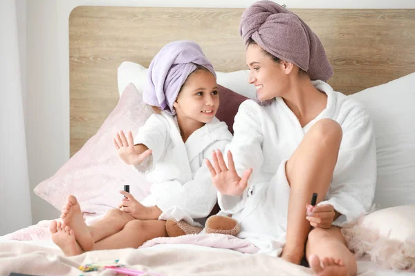 Mother and her little daughter in bathrobes manicuring nails in bedroom