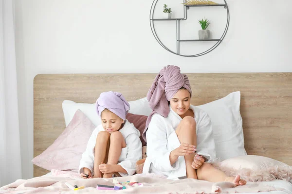 Mother and her little daughter in bathrobes doing pedicure in bedroom — Stock Photo, Image