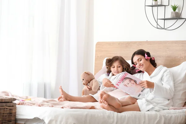 Mother and her little daughter in bathrobes and with fashion magazine relaxing at home — Stock Photo, Image