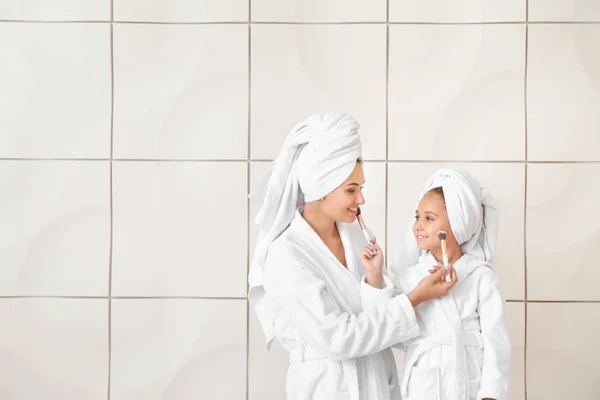 Mother and her little daughter in bathrobes applying makeup against white background — Stock Photo, Image