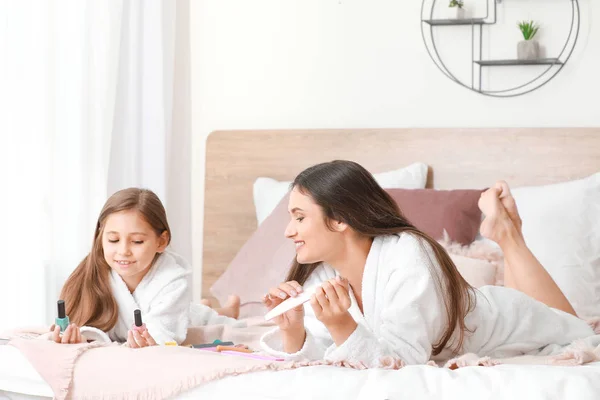 Mutter und ihre kleine Tochter in Bademänteln beim Nägelmachen im Schlafzimmer — Stockfoto