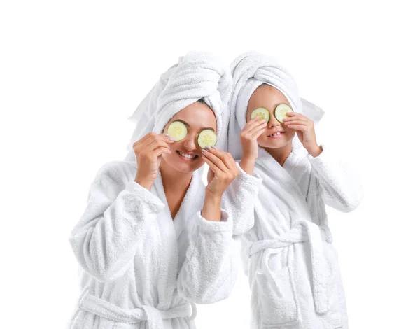 Mother and her little daughter in bathrobes and with cucumber slices on white background