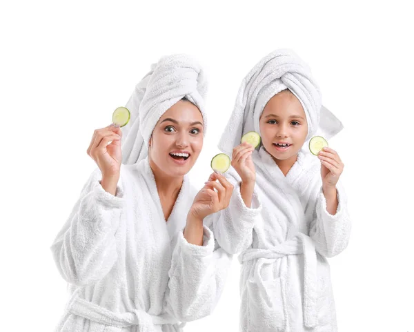 Mother and her little daughter in bathrobes and with cucumber slices on white background — Stock Photo, Image