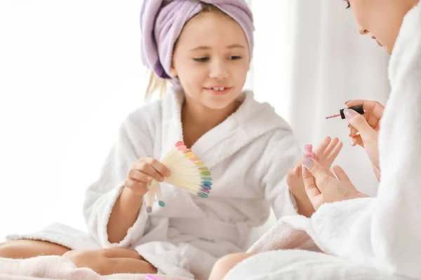 Mother and her little daughter in bathrobes manicuring nails in bedroom — Stock Photo, Image