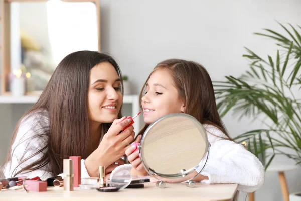 Мама и ее маленькая дочь в халатах наносят макияж дома — стоковое фото