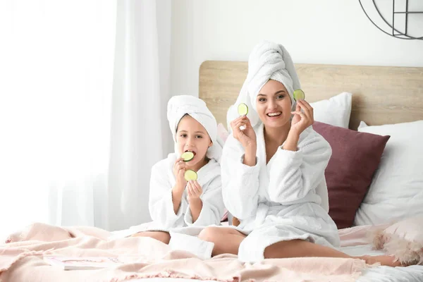 Madre y su hija pequeña en batas de baño y con rodajas de pepino en el dormitorio —  Fotos de Stock