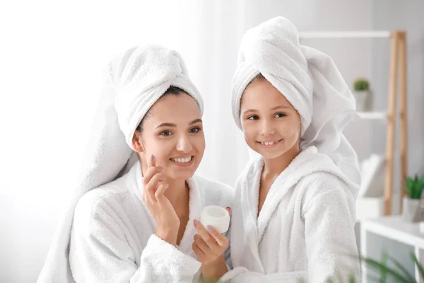 Mãe e sua filha em roupões de banho aplicando creme facial em casa — Fotografia de Stock