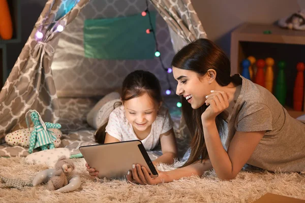 Mother and her little daughter with tablet computer at home in evening — Stock Photo, Image