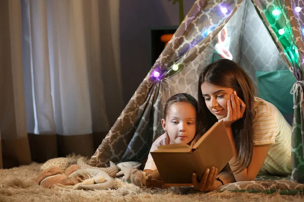 Mother and her little daughter reading book at home in evening — Stock Photo, Image