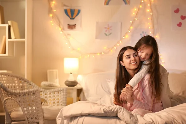 Happy woman with her little daughter on bed in evening — Stock Photo, Image