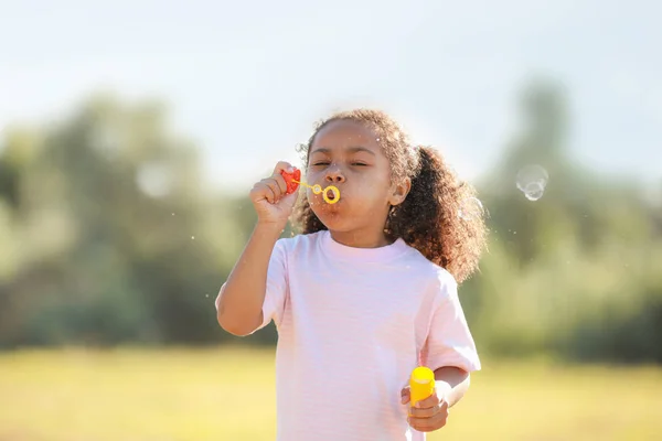 Cute African-American girl blowing soap bubbles outdoors — Stock Photo, Image