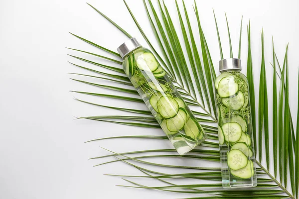 Bottles of infused water and palm leaf on light background — Stock Photo, Image