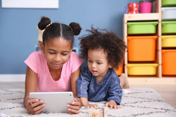 Cute African-American girl with tablet computer watching cartoons at home