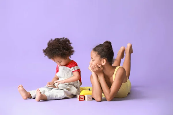 Cute African-American sisters with tablet computer watching cartoons on color background — Stock Photo, Image